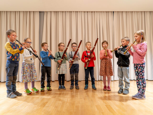 Bläserbande: Viele Kinder mit verschiedenen Blasinstrumenten in einem Halbkreis stehend