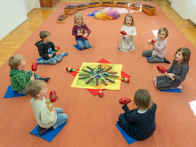 Kinder im Kreis sitzend mit Rasseln