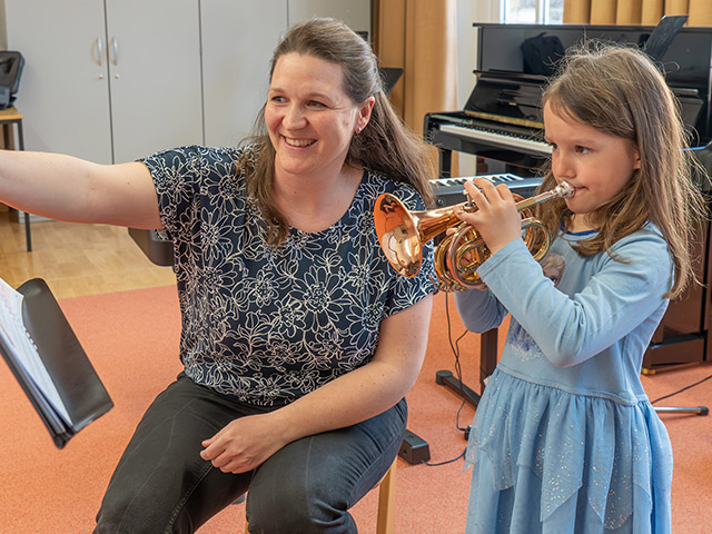 Musiklehrerin zeigt auf Notenblätter und Mädchen spielt auf Trompete