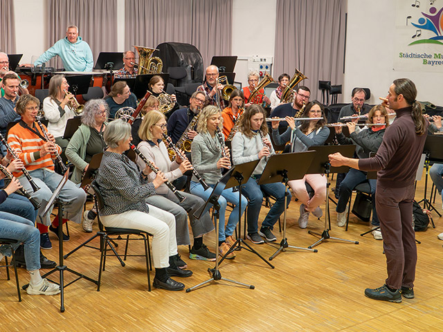 Viele Leute spielen verschiedene Blasinstrumente vor einem Dirigenten - Blasorchester