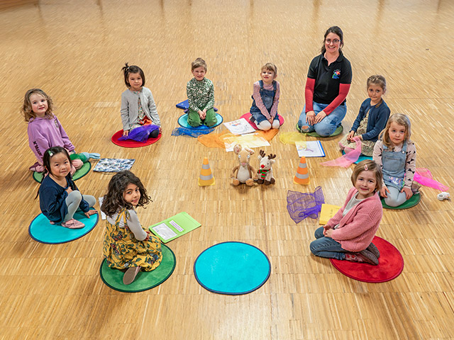 Chorzwerge: Kinder sitzen im Kreis auf dem Boden mit Musiklehrerin