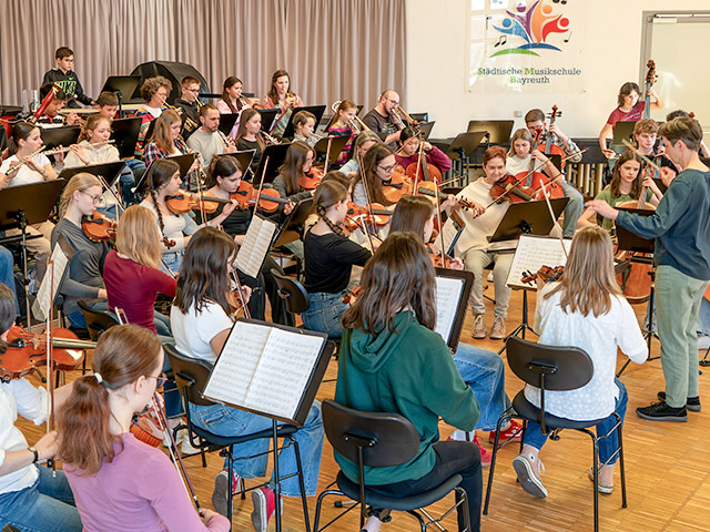 Viele Leute spielen verschiedene Instrumente vor einer Dirigentin - Sinfonieorchester